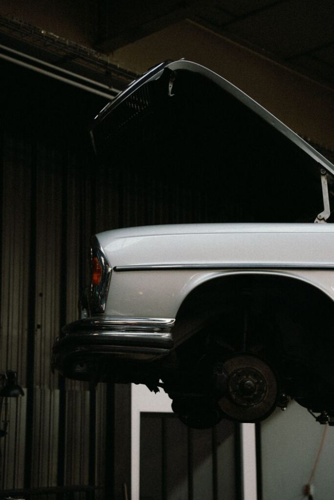 Close-up of a vintage car with hood open, undergoing repair in a garage setting.