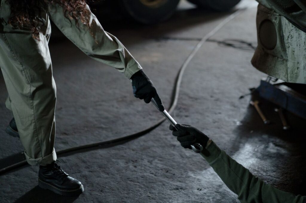 Two mechanics exchanging a wrench in a workshop, highlighting teamwork and skill.